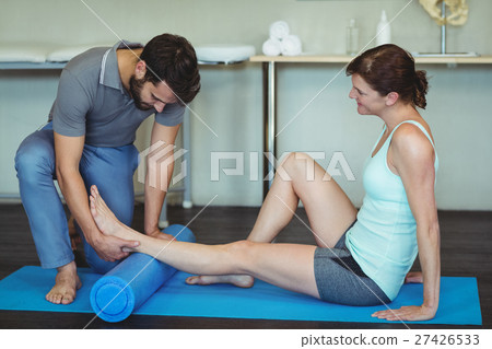 Physiotherapist giving leg massage to a woman on exercise mat 27426533