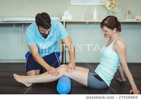 Physiotherapist doing leg therapy to a woman using foam roll 27426669