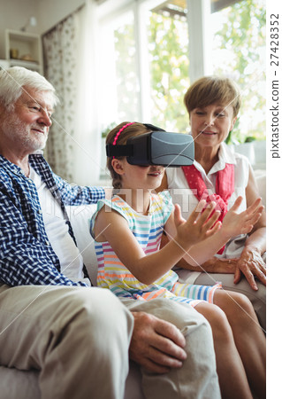 Granddaughter using virtual reality headset with her grandparents in living room 27428352