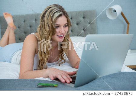 Woman using laptop on bed in bedroom Woman using laptop on bed in bedroom 27428673