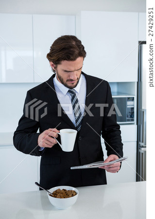 Businessman reading newspaper while having coffee in kitchen Businessman reading newspaper while having coffee in kitchen 27429251