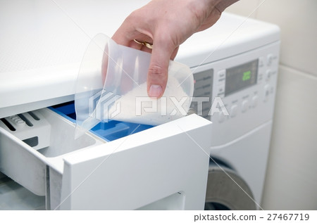 Hand pouring washing powder into washing machine 27467719