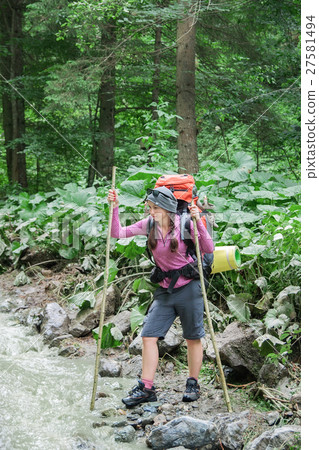 Hiker  with backpack crossing the mountain river 27581494
