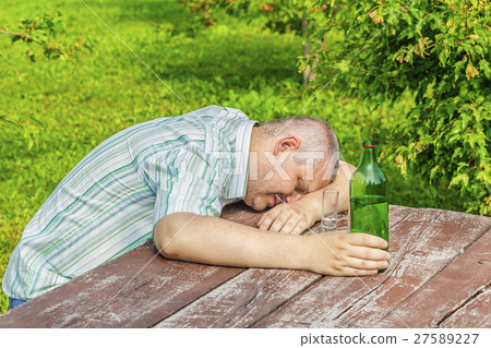 Drunk man sleeping near bottle of alcohol on table 27589227