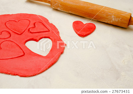 Red dough with a rolling pin and cut out hearts 27673431