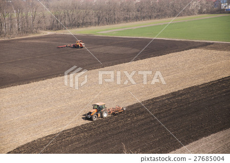 Tractor plows a field in the spring accompanied by 27685004