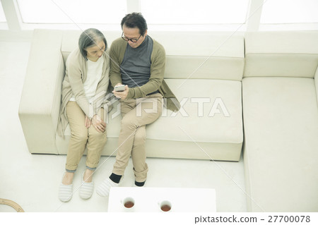 A couple sitting on a sofa and using a smartphone 27700078