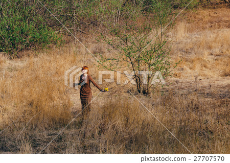 Young woman walking in golden dried grass field 27707570