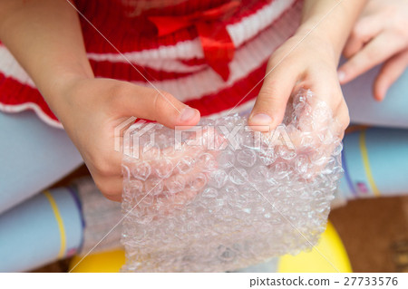 Top view of the child's hands pressing the bubbles on the packaging film 27733576