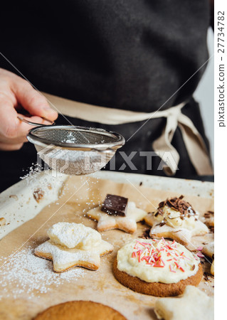 Person decorating cookies with toppings 27734782