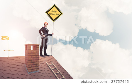 Young businessman on house brick roof holding yellow signboard. 27757445