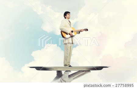Businessman on metal tray playing acoustic guitar against blue sky background Businessman on metal tray playing acoustic guitar against blue sky background 27758995