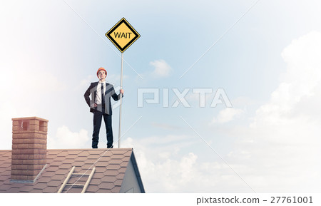 Young businessman on house brick roof holding yellow signboard. Young businessman on house brick roof holding yellow signboard. 27761001