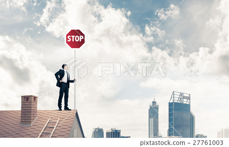 Caucasian businessman on brick house roof showing stop road sign Caucasian businessman on brick house roof showing stop road sign 27761003
