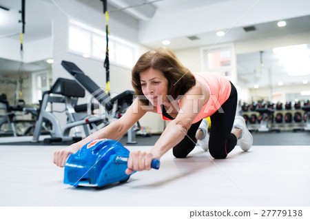 Senior woman in gym exercising abs with wheel 27779138
