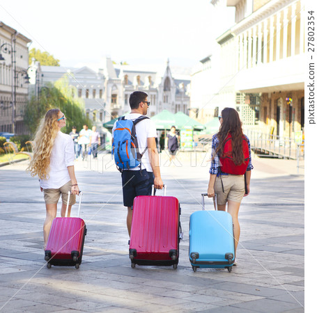 Travelers friends with luggage walking by street  27802354