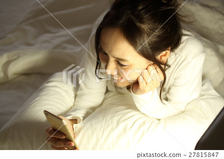 A girl watching a smartphone in a futon 27815847