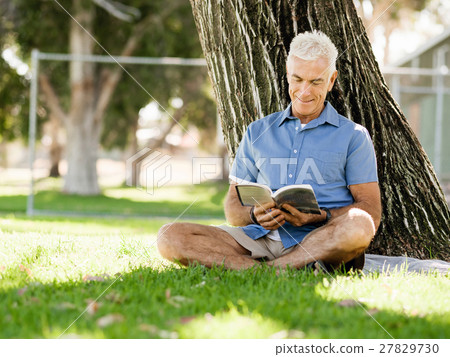 Senior man sittingin park while reading book Senior man sittingin park while reading book 27829730