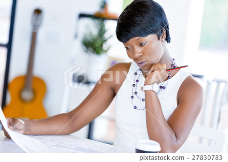 Young woman sitting at a desk in an office and working on blueprint 27830783
