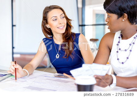 Young women sitting at a desk in an office and working on blueprint Young women sitting at a desk in an office and working on blueprint 27831689