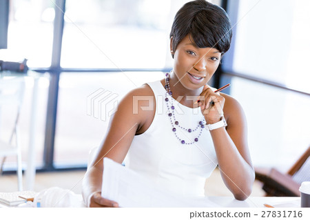 Young woman sitting at a desk in an office and working on blueprint 27831716