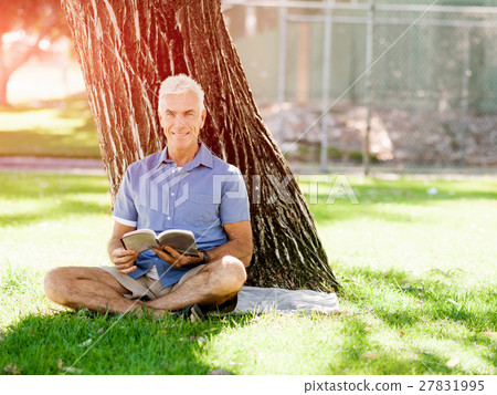Senior man sittingin park while reading book Senior man sittingin park while reading book 27831995