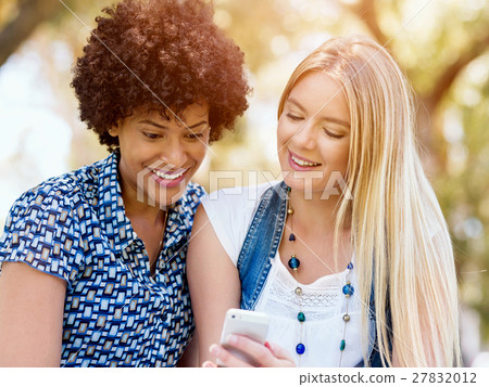 Two women friends in park with mobile phone Two women friends in park with mobile phone 27832012