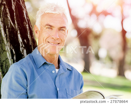 Senior man sittingin park while reading book Senior man sittingin park while reading book 27878664