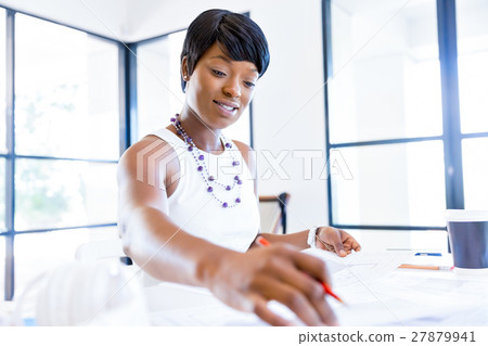 Young woman sitting at a desk in an office and working on blueprint Young woman sitting at a desk in an office and working on blueprint 27879941