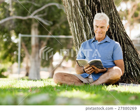 Senior man sittingin park while reading book Senior man sittingin park while reading book 27880269