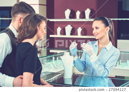 Smiling seller showing necklace for buyers at 27894127