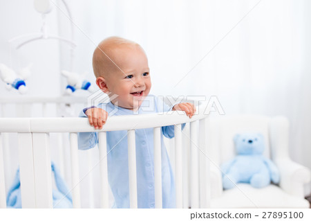 Baby boy standing in bed in white nursery 27895100