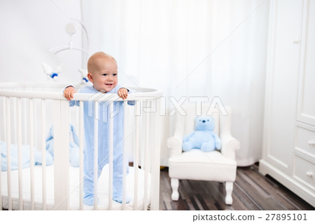 Baby boy standing in bed in white nursery 27895101