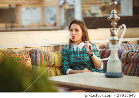Beautiful young woman smokes a hookah in a cafe 27915646