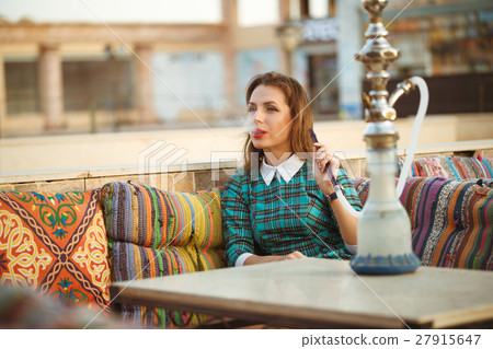 Beautiful young woman smokes a hookah in a cafe 27915647