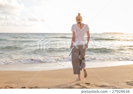 Woman walking on sand beach at golden hour 27926636