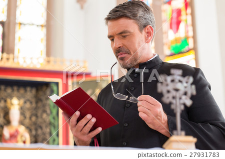 Priest reading bible in church standing at altar 27931783