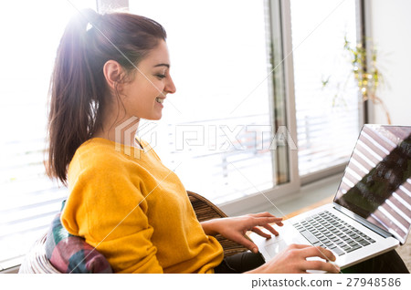 Woman at home sitting on sofa, working on laptop 27948586