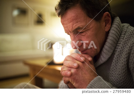 Senior man at home praying, burning candles behind Senior man at home praying, burning candles behind 27959480