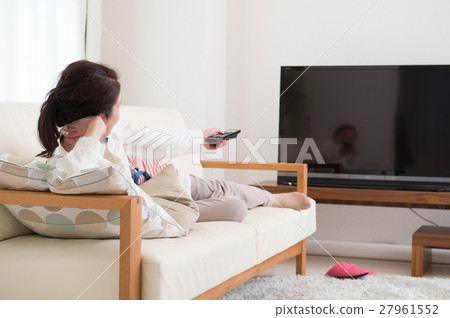 A middle-aged woman watching TV while lying on the sofa A middle-aged woman watching TV while lying on the sofa 27961552