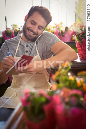 Male florist noting order in dairy while talking on mobile phone Male florist noting order in dairy while talking on mobile phone 27963540