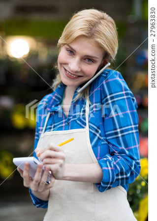 Female florist taking order on mobile phone in flower shop 27963830