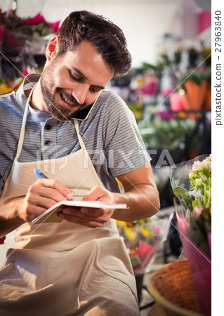 Male florist noting order in diary while talking on mobile phone Male florist noting order in diary while talking on mobile phone 27963840