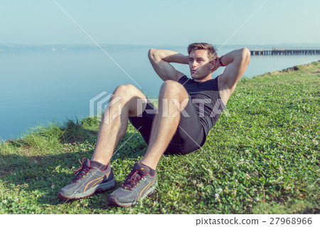 Sporty young man doing sit-ups abs crunches Sporty young man doing sit-ups abs crunches 27968966