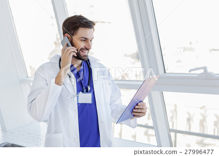 Happy male general practitioner talking on mobile 27996477
