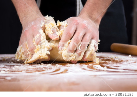 Male baker kneading dough on flour covered table 28051185