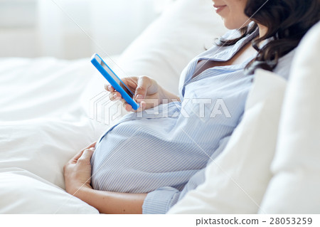 close up of pregnant woman with smartphone in bed close up of pregnant woman with smartphone in bed 28053259