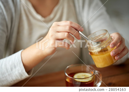 close up of woman adding honey to tea with lemon close up of woman adding honey to tea with lemon 28054163