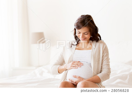 happy pregnant woman sitting on bed at home happy pregnant woman sitting on bed at home 28056828
