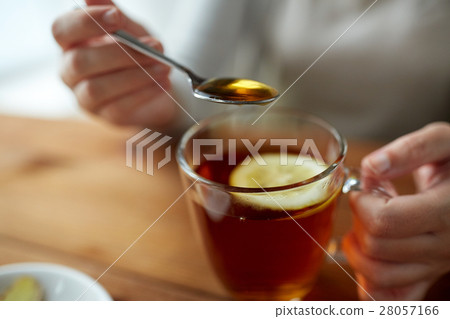 close up of woman adding honey to tea with lemon 28057166